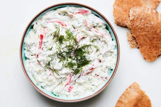 Cucumber spread with tomatoes in a bowl, garnished with fresh dill. There are pieces of bread next to it.