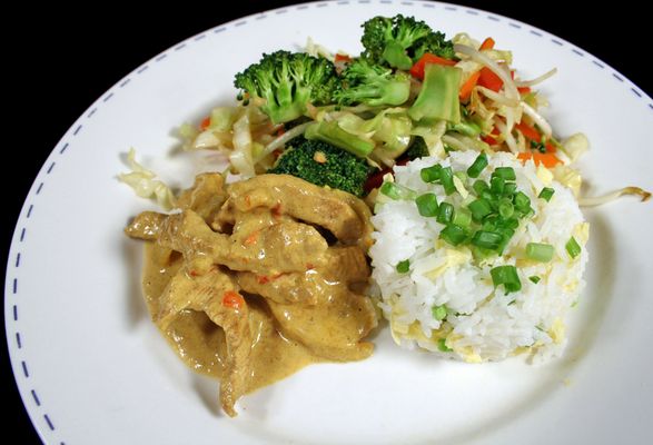 Vepřové maso s kari omáčkou, rýží a zeleninou na talíři.