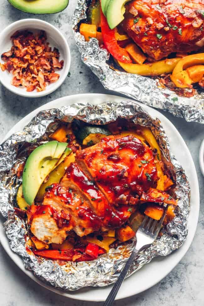 Chicken marinated in BBQ sauce grilled with vegetables in foil with a fork and a slice of avocado.