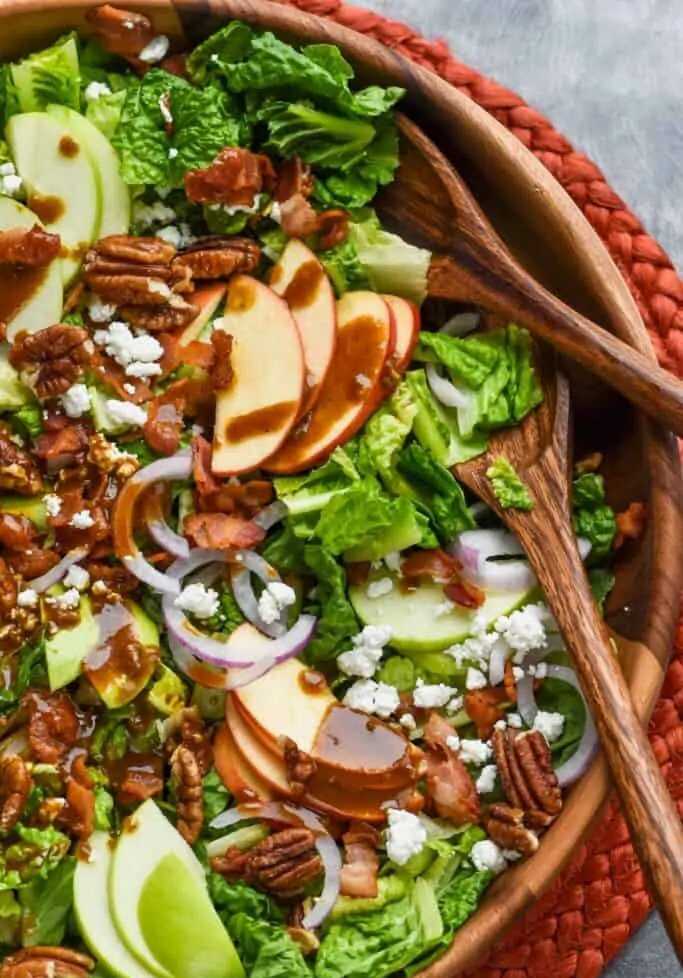 Apple, bacon, pecan and goat cheese salad in a bowl with wooden spoons.
