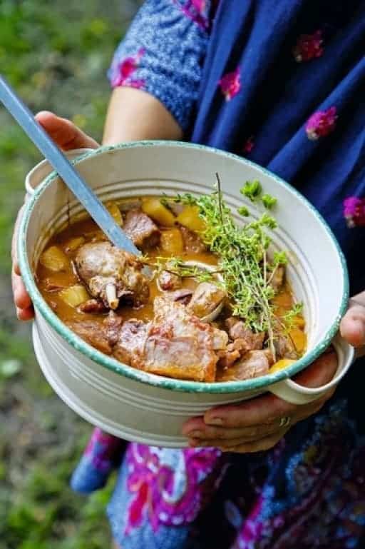 Duck stew with vegetables in a pot held by a woman.