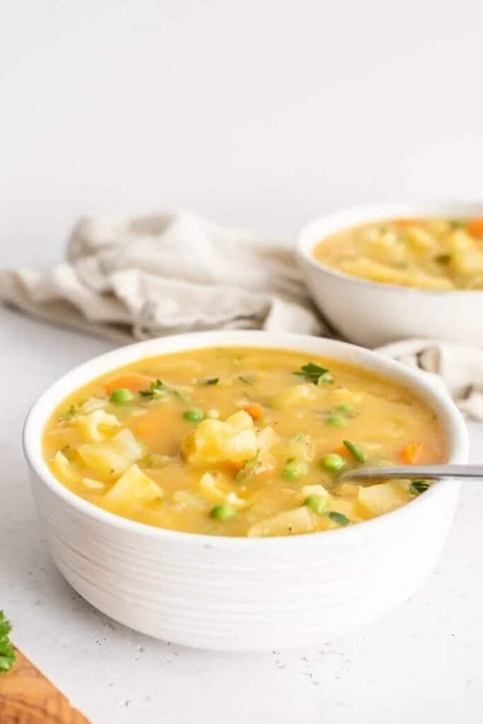 Cauliflower and potato soup with peas in a bowl with a spoon.