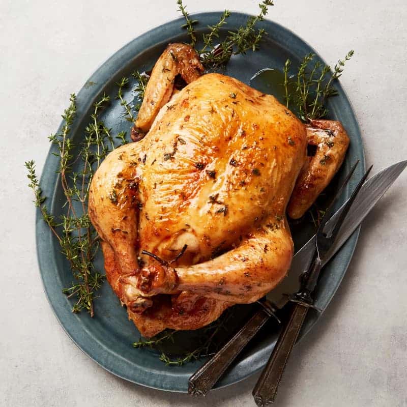 Upečené kuře na tymiánu na velkém talíři s příborem.