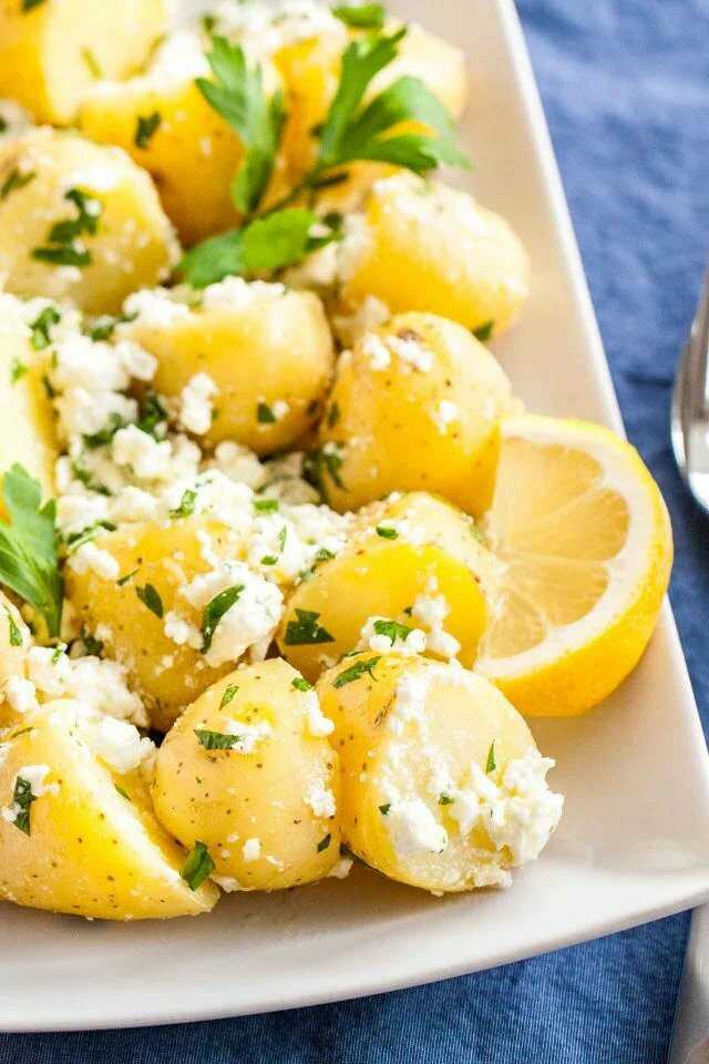 Potatoes with feta, herbs and a lemon wedge on a plate.