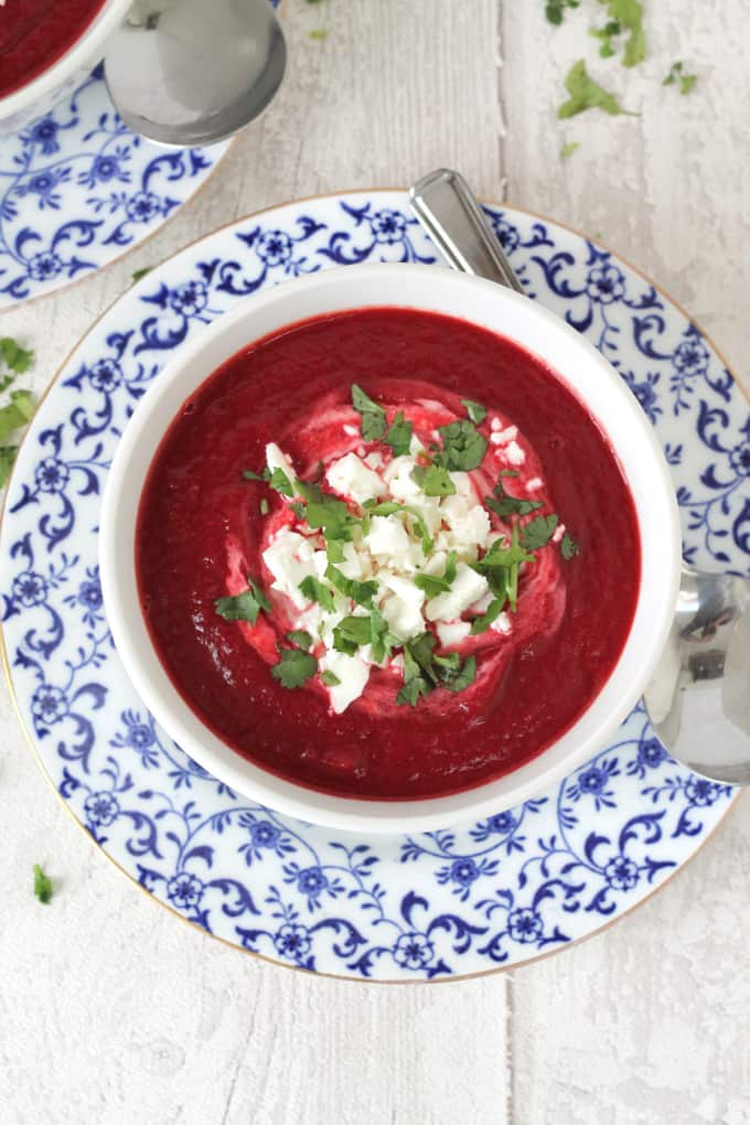 Beetroot, carrot and potato soup, garnished with creme fraiche, parsley and crumbled feta cheese on a deep plate.