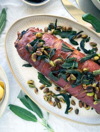 Roll of prosciutto, ground turkey and stuffing on a tray, decorated with pistachios and sage.