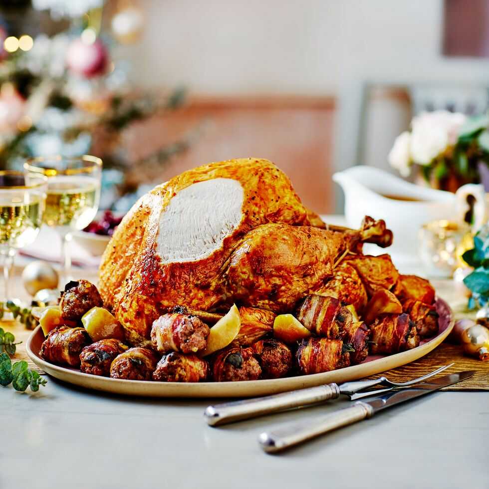 Turkey with baked apples and stuffing in bacon on a large plate with cutlery placed next to it.