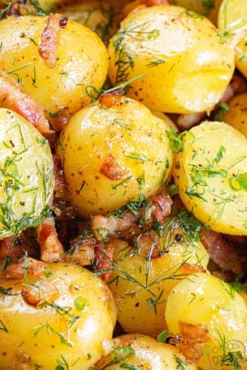 Potatoes in butter sauce with bacon and onions garnished with fresh herbs.