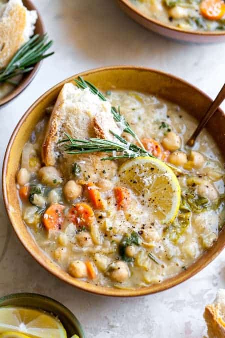 Bean soup with vegetables in a deep plate, decorated with a slice of lemon and herbs.