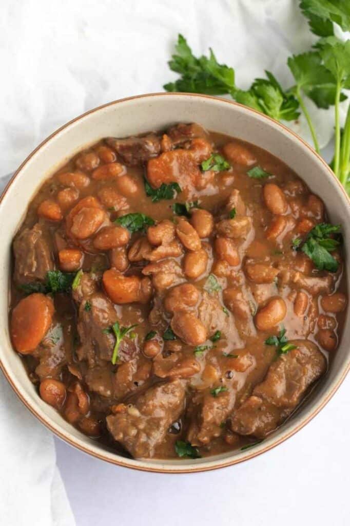 Beef stew with beans in a large pot, garnished with fresh herbs.