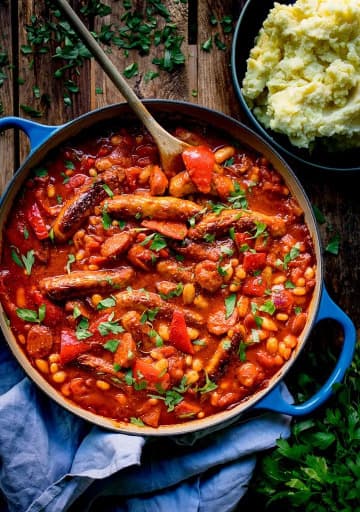Bean stew with sausages in a large pot with a wooden spoon.