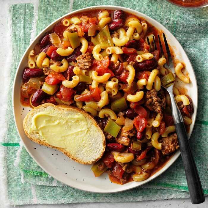 Bean and minced meat stew served with pasta and a slice of buttered bread on a plate with a fork.