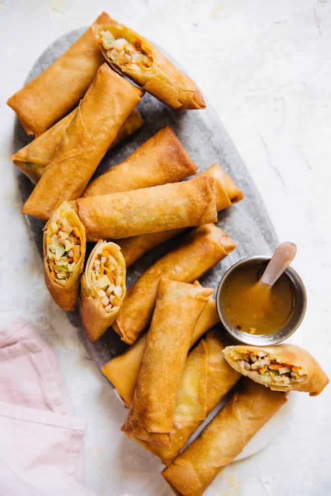 Chinese spring rolls filled with vegetables and minced meat served with a bowl of sauce.