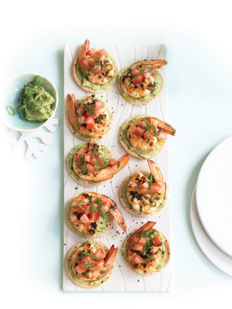 Small tortillas with mashed avocado, grilled shrimp and tomato salsa served on a long tray.