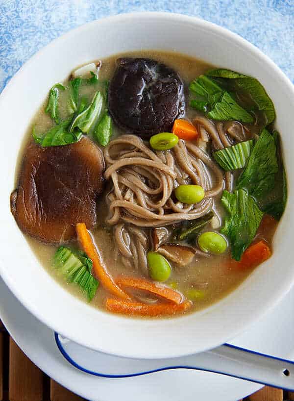 Japanese soup with mushrooms, buckwheat noodles, soybeans, carrots and salad in a deep plate.