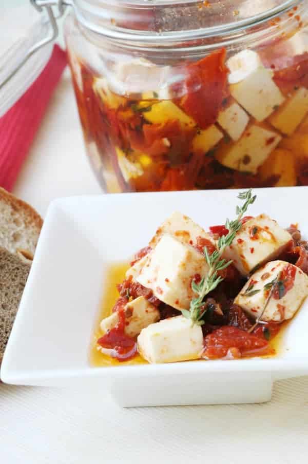 Beladener Käse mit Kräutern und sonnengetrockneten Tomaten auf einem Teller und in einem Glas.