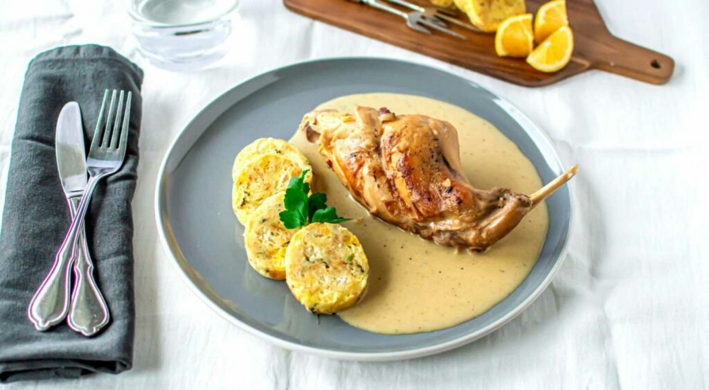 Rabbit with cream sauce and dumpling on a plate. Cutlery is placed next to it.