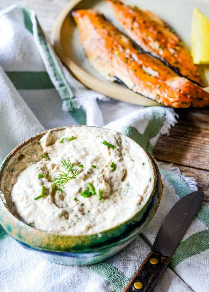Mackerel dip in a bowl, decorated with fresh herbs. A knife is placed next to it.