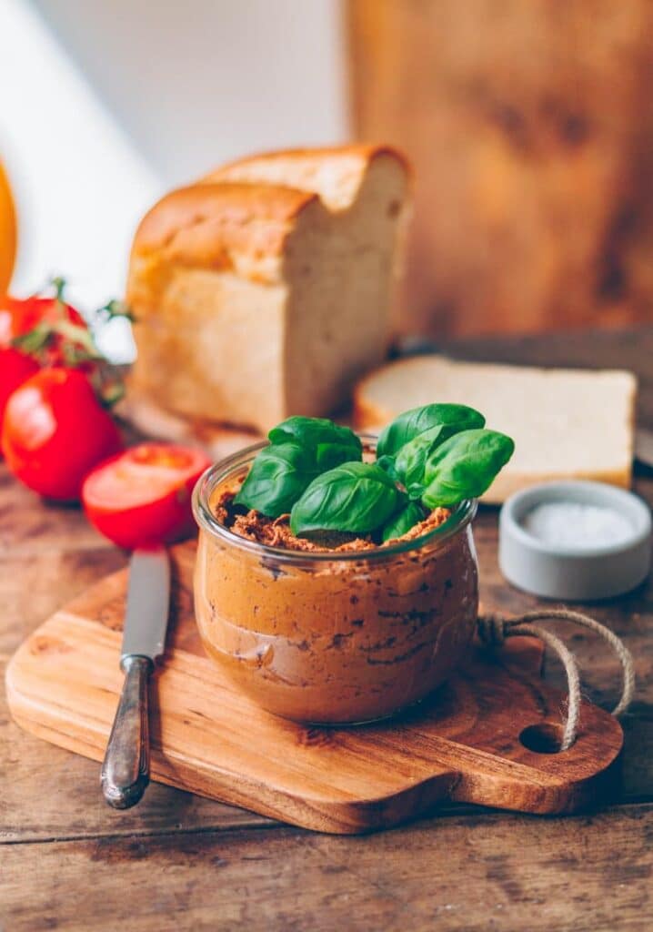 Tomato dip in a jar, garnished with basil and served on a board.