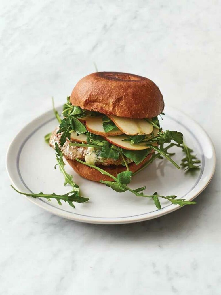 Burger with pork, blue cheese, sweet pear and leafy greens on a plate.