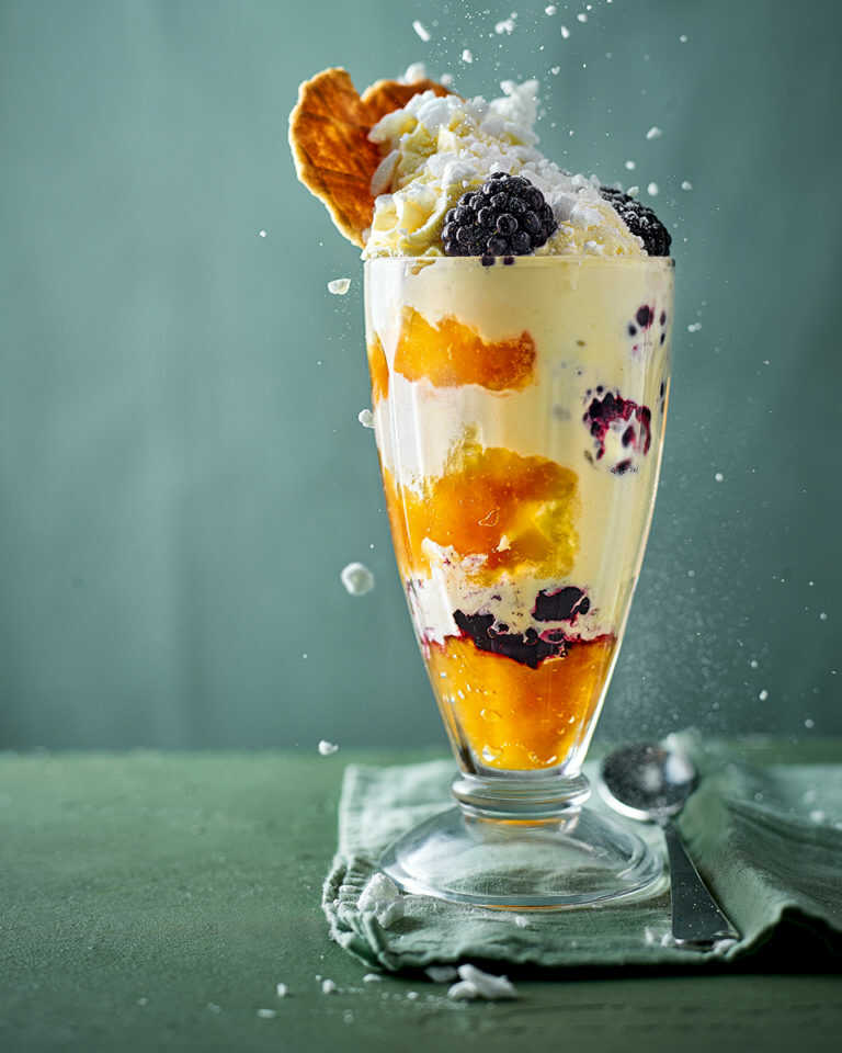 Ice cream sundae with fresh blackberries, snow meringue and home-canned peaches in a large wafer glass.