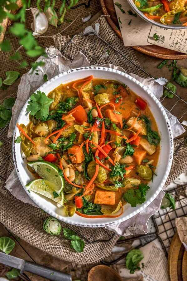 Curry soup with vegetables in a deep plate, garnished with fresh herbs and lime wedges.