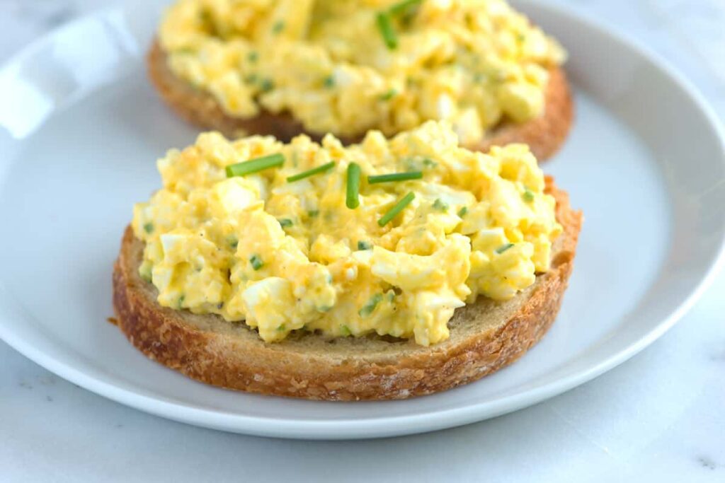 Egg salad spread on slices of bread and garnished with fresh chives.
