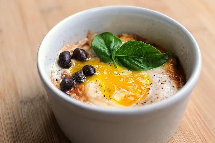 A baked ramekin with eggs, beans and cheese, garnished with fresh basil.