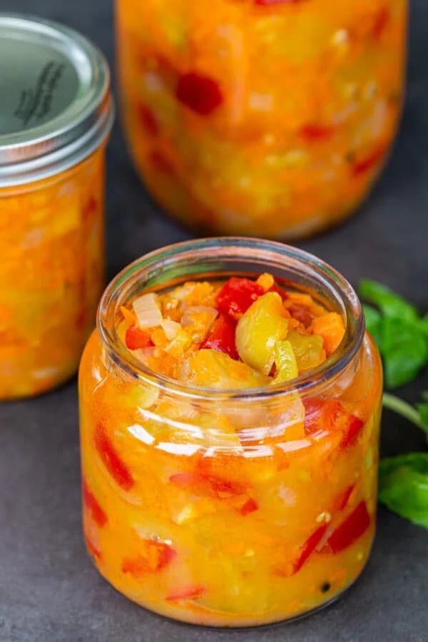 Canned salad of green tomatoes, red peppers and carrots in jars.