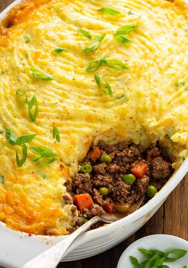 Meat with vegetables in a rich sauce, baked with a pillow of potatoes and cheese in a baking dish with a spoon.