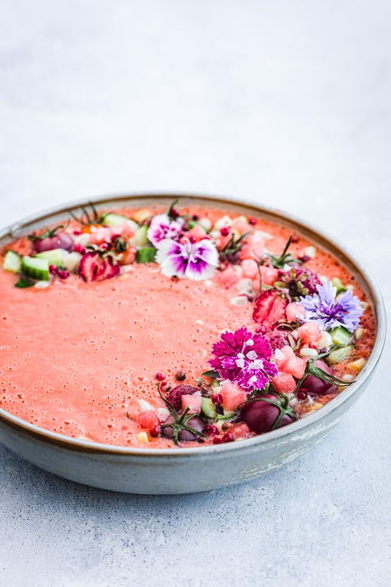 Ružová studená polievka ozdobená kvetmi a paradajkami.