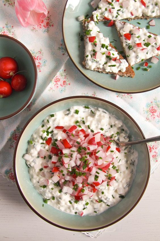 A bowl full of creamy spread of cheese and sour cream decorated with chives and radish.