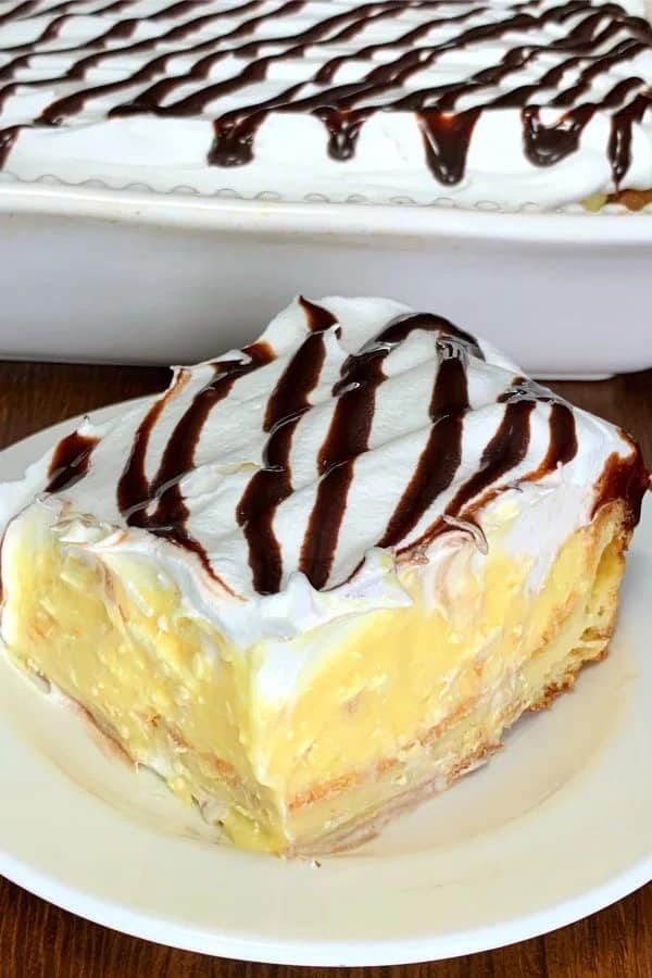 Slices with a creamy custard filling and topped with whipped cream with chocolate syrup served on a plate.