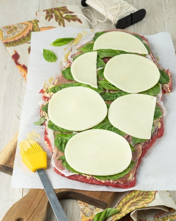 Rozprostřený plátek masa naplněný zelenou rukolou a sýrem.