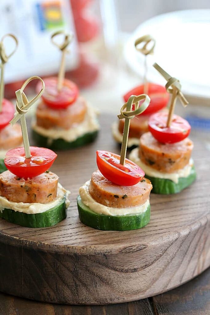 Plátky uhorky obložené klobásou, hummusom a cherry paradajkou.