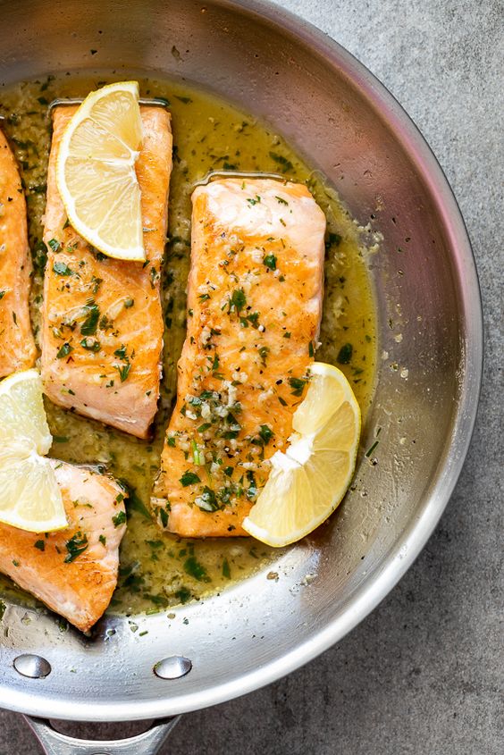 Pieces of perfect salmon in a wine sauce with lemon wedges.