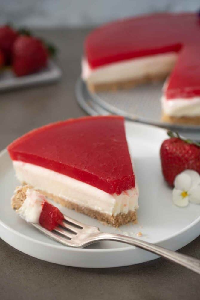 Cheesecake necoaptă cu glazură de gelatină de căpșuni pe o farfurie cu o furculiță.