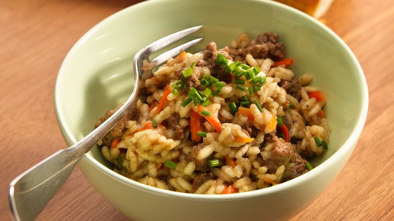 Reis mit sautiertem Hackfleisch, geriebenen Karotten und Käse, garniert mit frischem Schnittlauch und in einer Schüssel mit einer Gabel serviert.