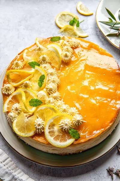 Cheesecake s krémem lemon curd a šlehačkou, ozdobený plátky citronu a čerstvou mátou na talíři.