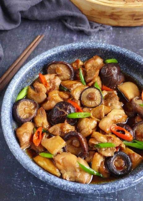 Čínské dušené kuřecí maso s houbami shiitake v misce s vedle položenými hůlkami.