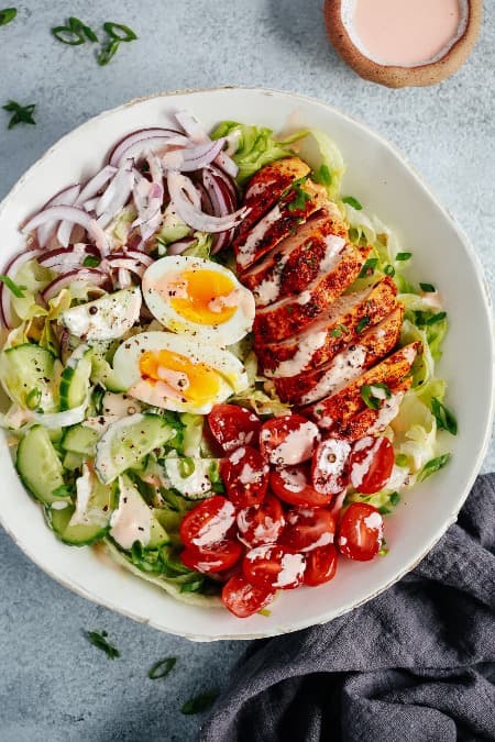 Hühnersalat mit Salat, Gurke, Kirschtomaten, roten Zwiebeln, gekochtem Ei und köstlichem würzigem Mayonnaise-Dressing auf einem Teller.