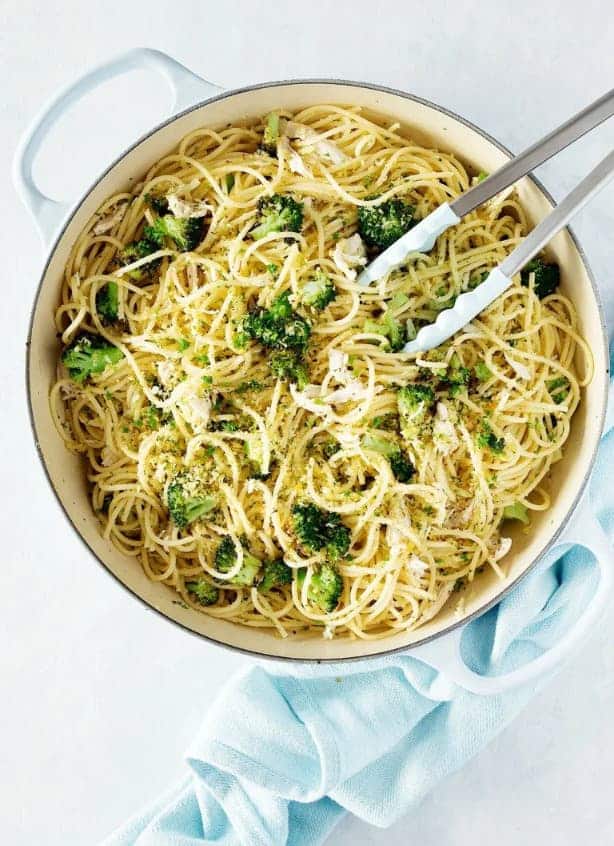 Špagety s česnekem, kuřecím, brokolicí, sardelovými filety a strouhankou v hrnci s kleštěmi.