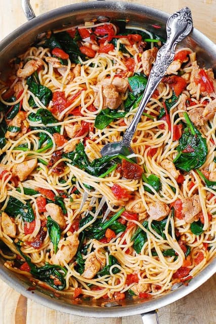Špagety s čerstvými a sušenými rajčaty, bazalkou, špenátem, česnekem, kuřecím masem a olivovým olejem v hrnci s vidličkou