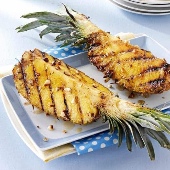 Ogrilovaný čerstvý ananas politý máslem s javorovým sirupem a posypaný ořechy na talíři.