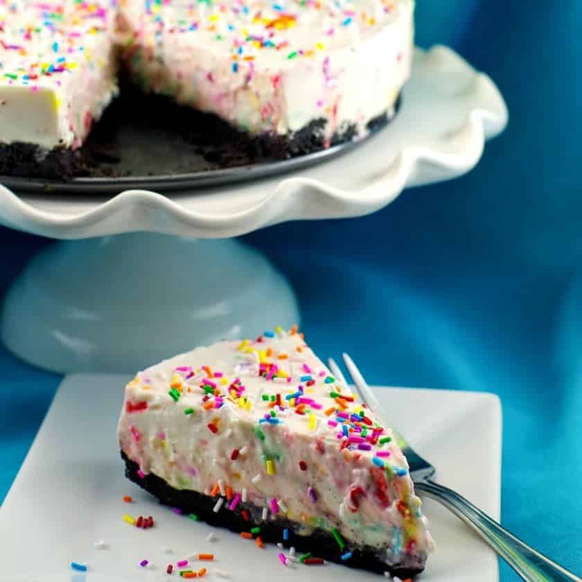 Kus nepečeného narozeninového dortu s posypkami na talířku s vidličkou.