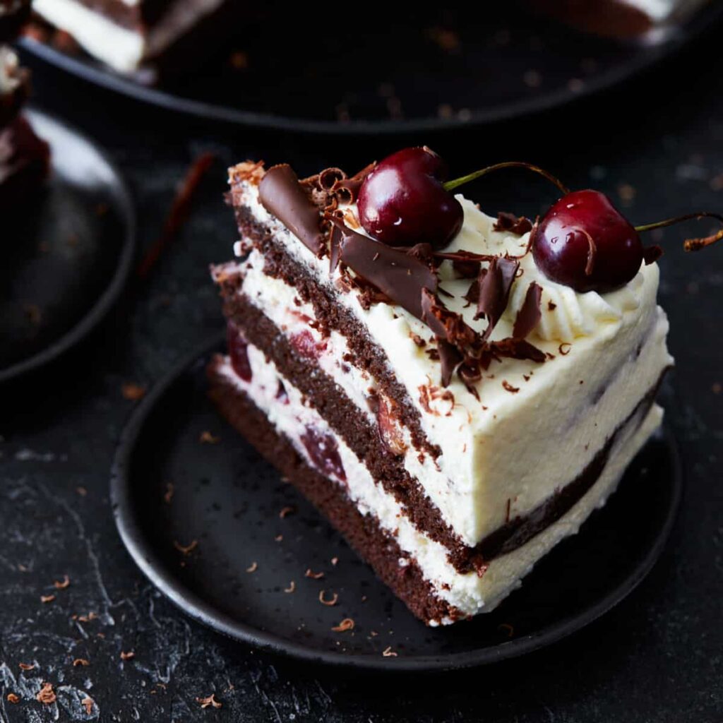 Kus čokoládového dortu se šlehačkou a višněmi na talířku.