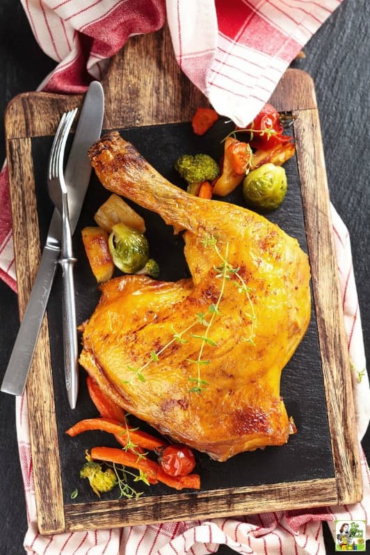 Vyuzené kuřecí stehno na prkýnku s příborem a zeleninou.