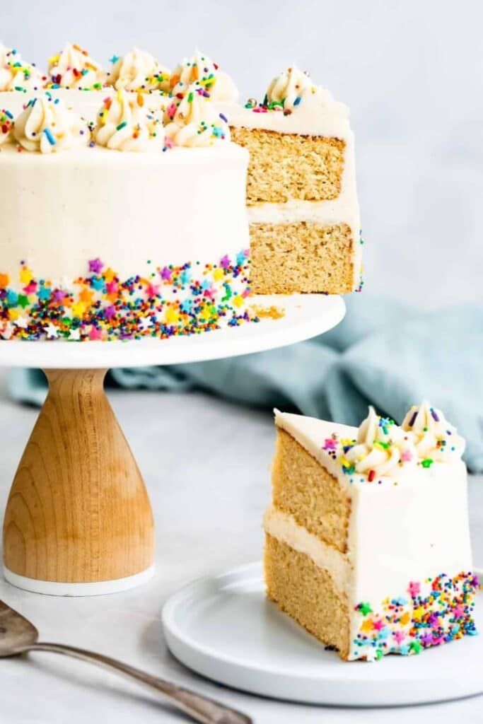 Vanilkový dort bez lepku na dortovém stojanu, ozdobený cukrářskými posypkami. 